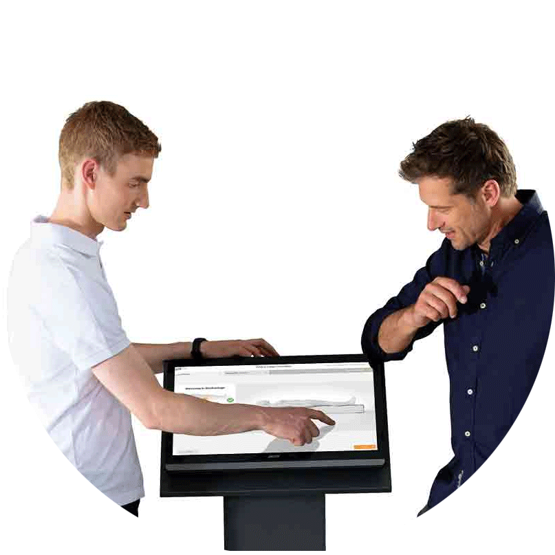 Liegedruckmessung: ein Berater und ein Kunde stehen an einem Mess-Terminal mit Touchscreen und sehen sich das Ergebnis der Messung an